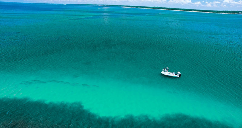 Anglers fly fishing on a small boat in a deep emerald sea.