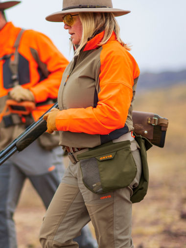 A hunter carries her shotgun threaded through her right arm.