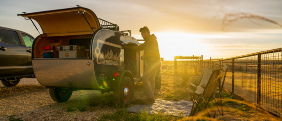 A camper unpacks his small trailer as the sun sets.