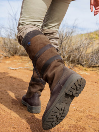 A hunter's high boots walk across red dirt.