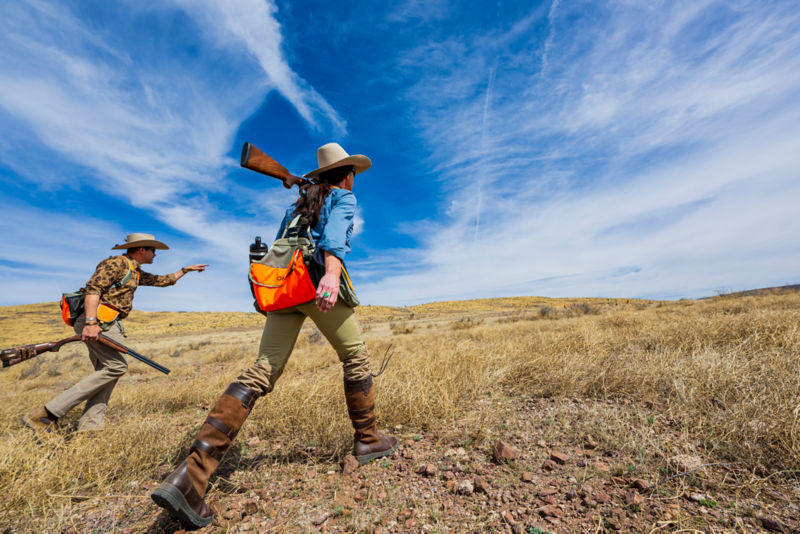 Two hunters climb a low hill under a dramatic cloud-filled sky.
