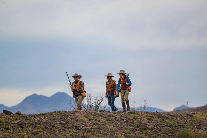 Three hunters walk side by side over rough terrain.