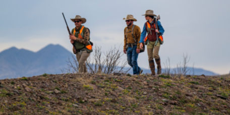 Three hunters walk side by side over rough terrain.