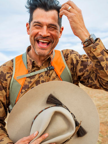 A hunter caught mid-laugh while removing his hat.