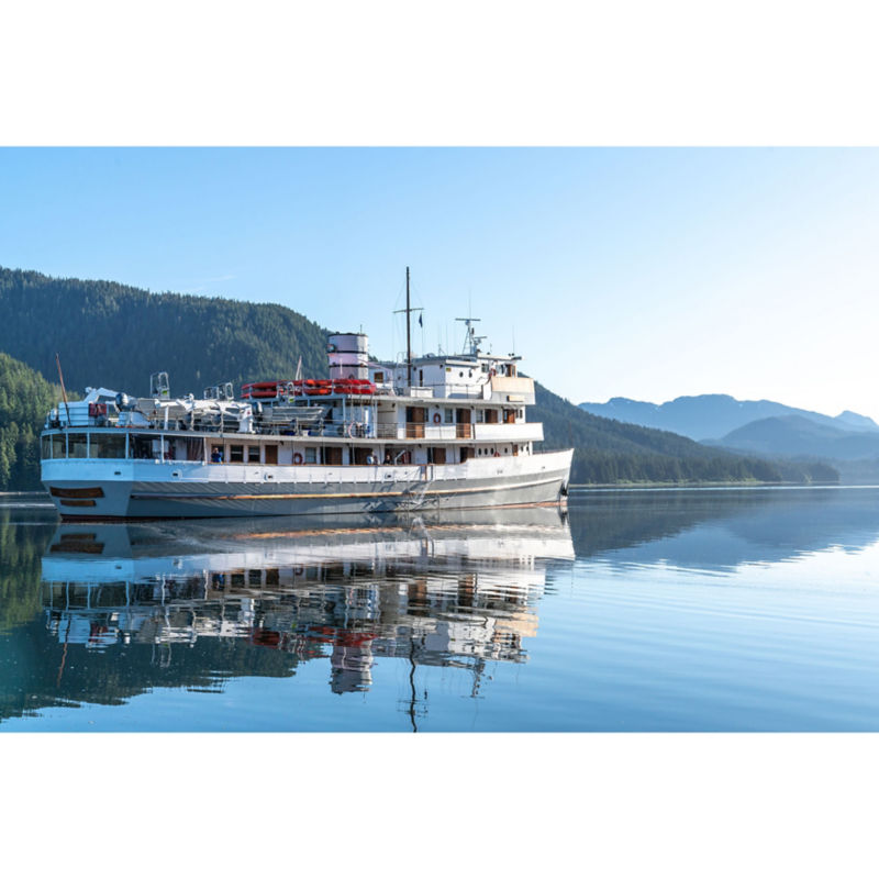 A small ship plies the waters of Alaska under snow-tipped mountains.