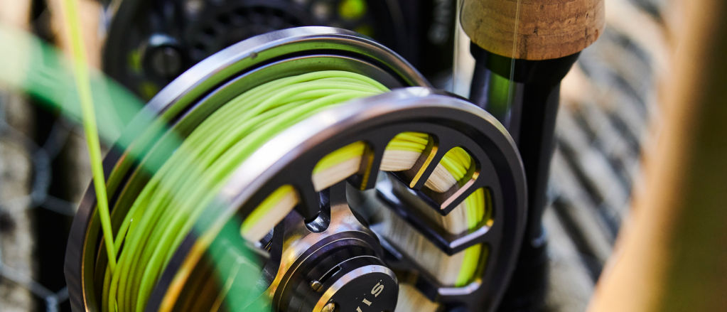 A close-up of the three fly-fishing reels on rods lined up along a fence.