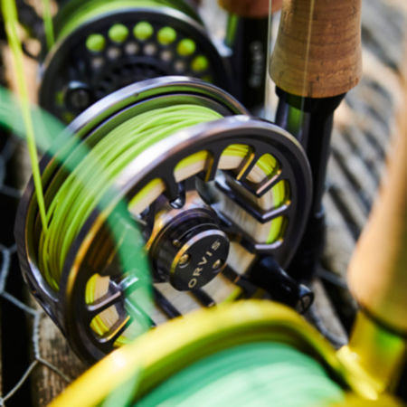A close-up of the three fly-fishing reels on rods lined up along a fance.