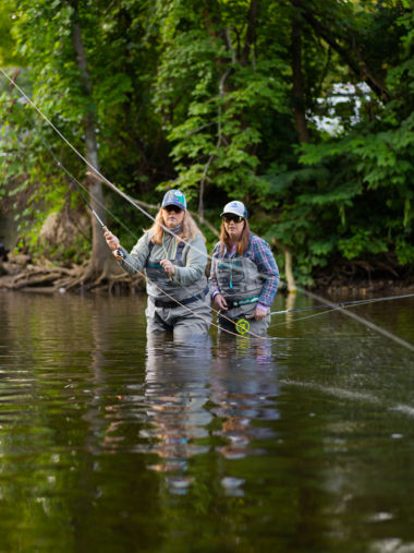 Two women standing in a river learning how to fly fish