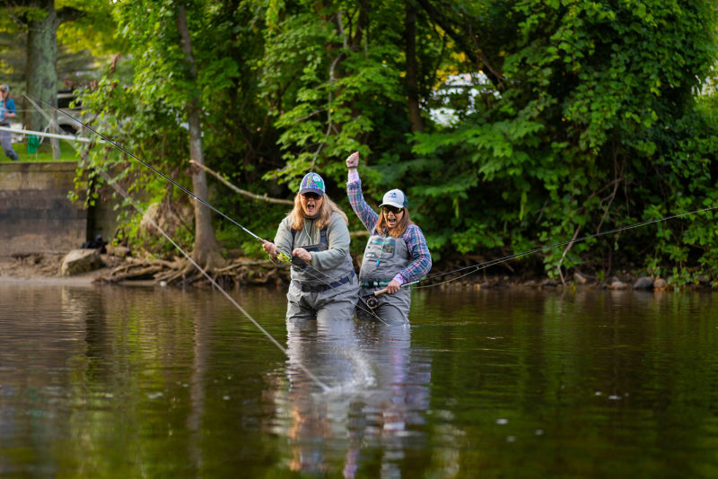 Two anglers in the water laughing and celebrating because one of them hooked a fish.