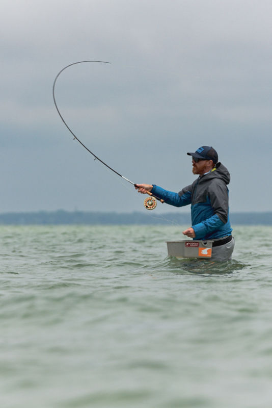 A saltwater fisherman casts his fly rod from waist-deep in the ocean.