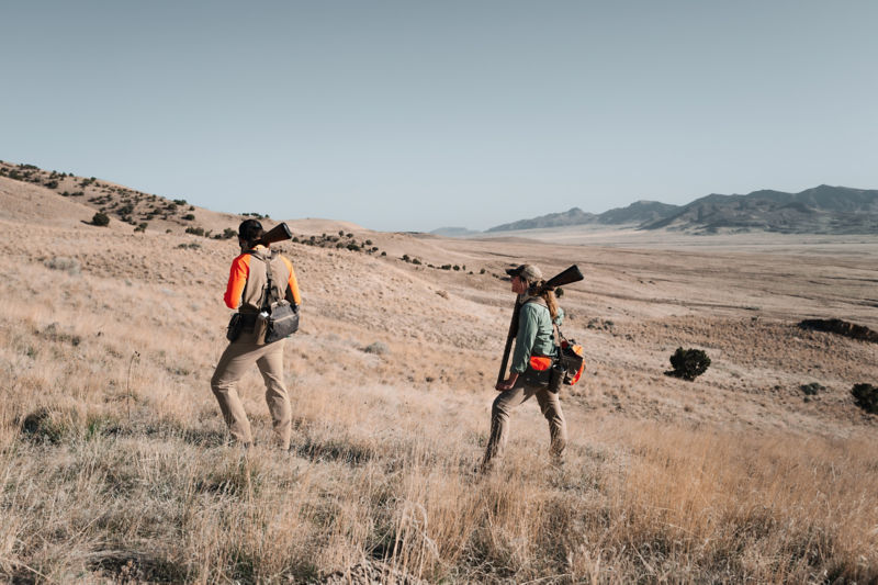 Two hunters wearing hunting vests hike the rolling hills of the midwest.