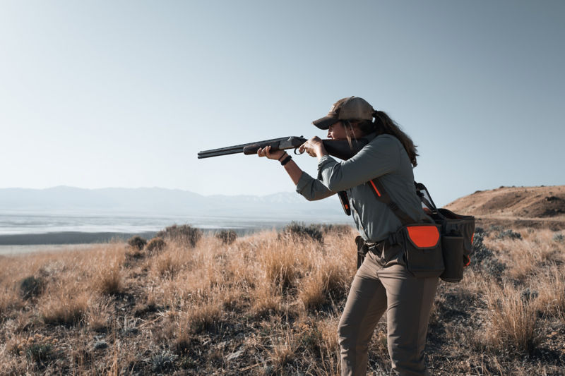 A hunter sets up for a shot on a hilly field of dry grass and rocks.