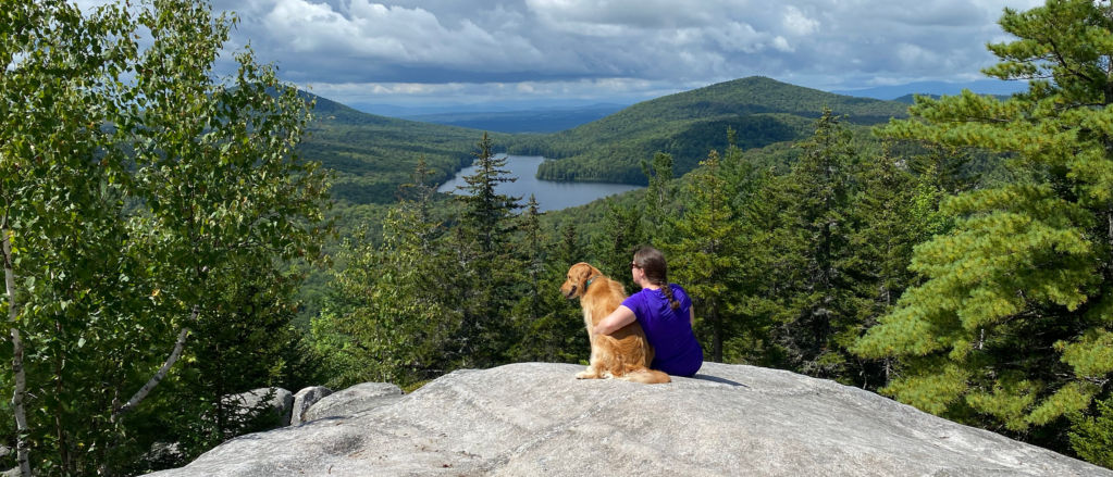A woman hugging her dog while sitting at the top of a mountain