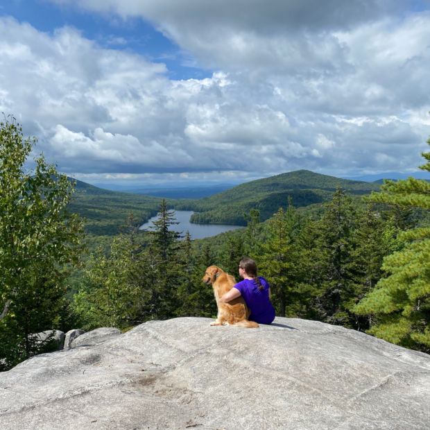 A hiker snuggles her dog at an overlook on a traill