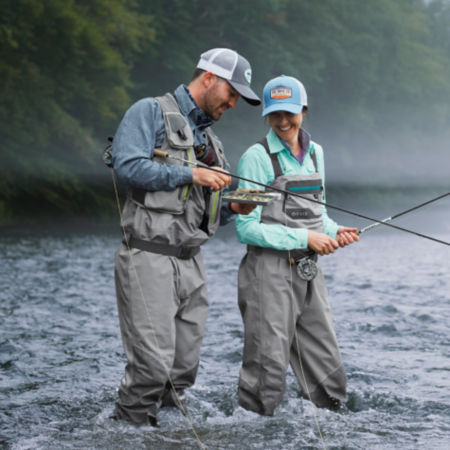 A guide helping a client choose the right fly while standing in a shallow river.