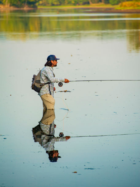 Man stands in a river during the summer drifting his fly and wearing an Orvis Guide Sling Pack