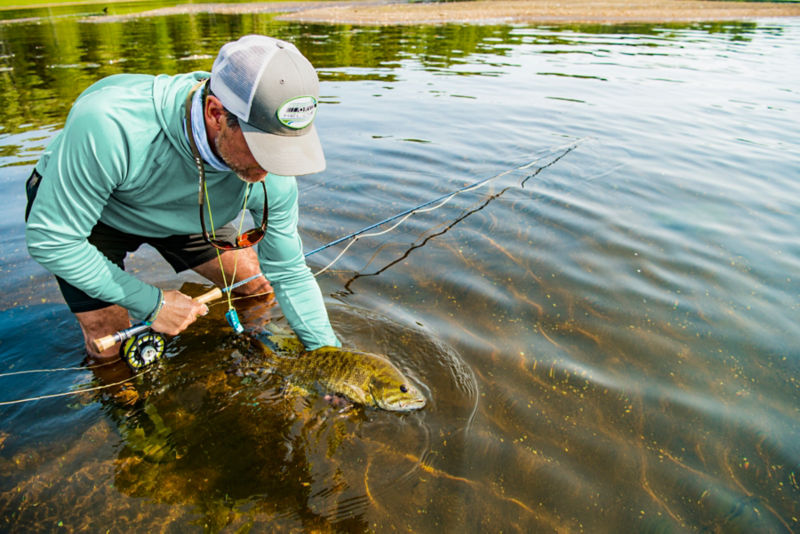Angler holds catch with rod half-submerged in river.
