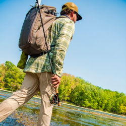 A man walking with fishing rod in hand while wearing an Orvis Bug-Out Backpack