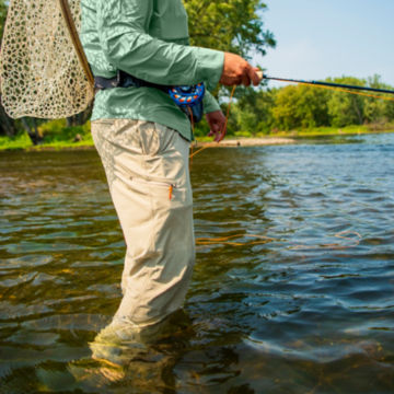 Angler wearing Canyon Jackson Quick-Dry Pants wades into river with his fishing gear.