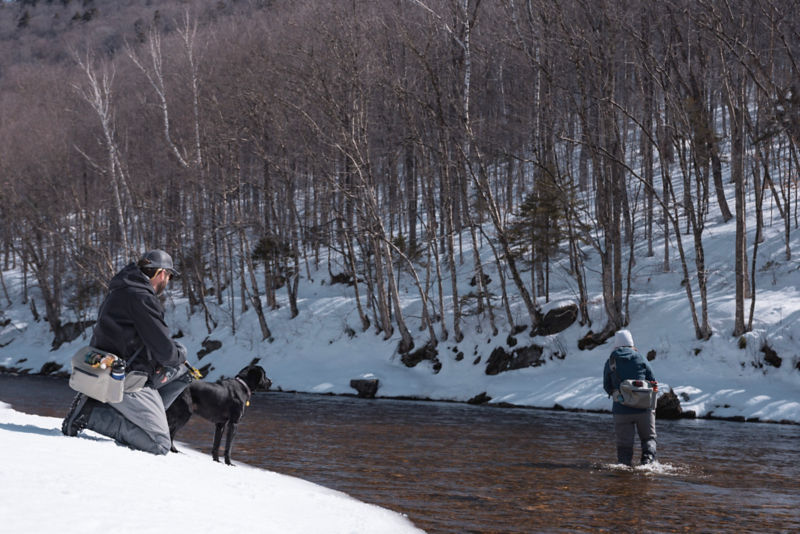Anglers fishing in the snow with their black labrador retriever.
