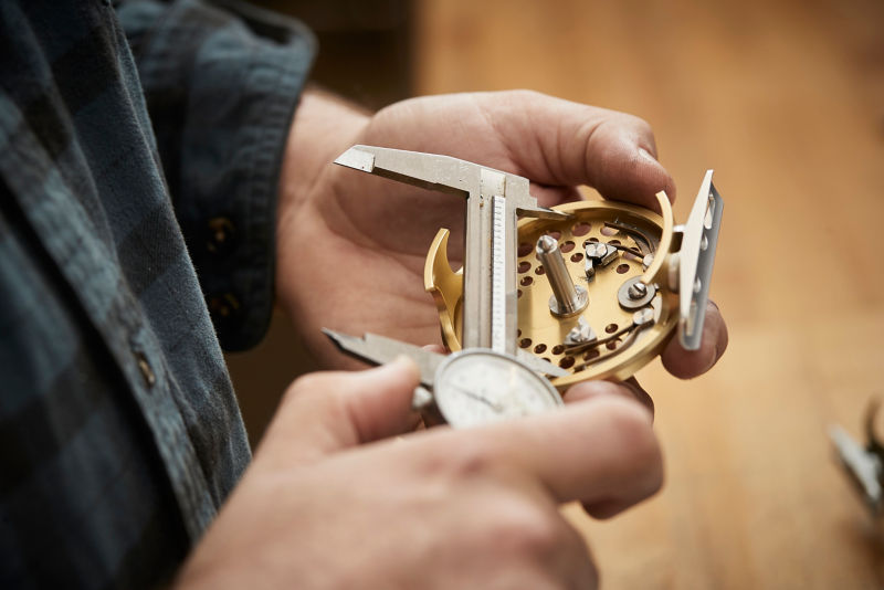A close-up of a hand holding part of a reel while the other hand uses calipers to measure.