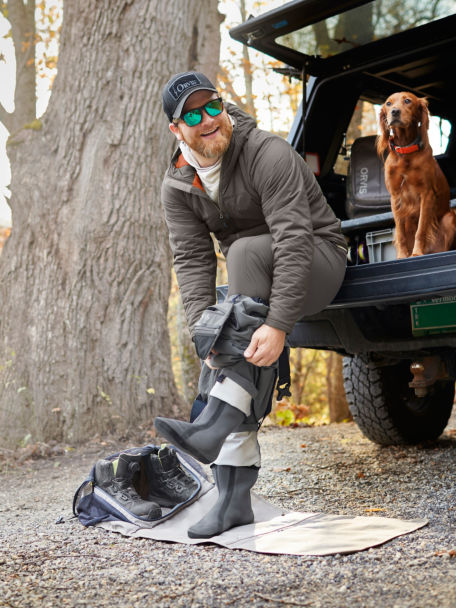 Man laughs alongside his dog as he pulls up his waders over his PRO Insulated Hoodie.