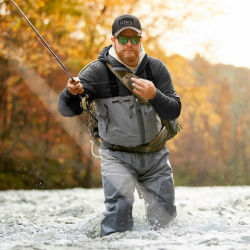 An angler wades knee-deep in a river on a fall day
