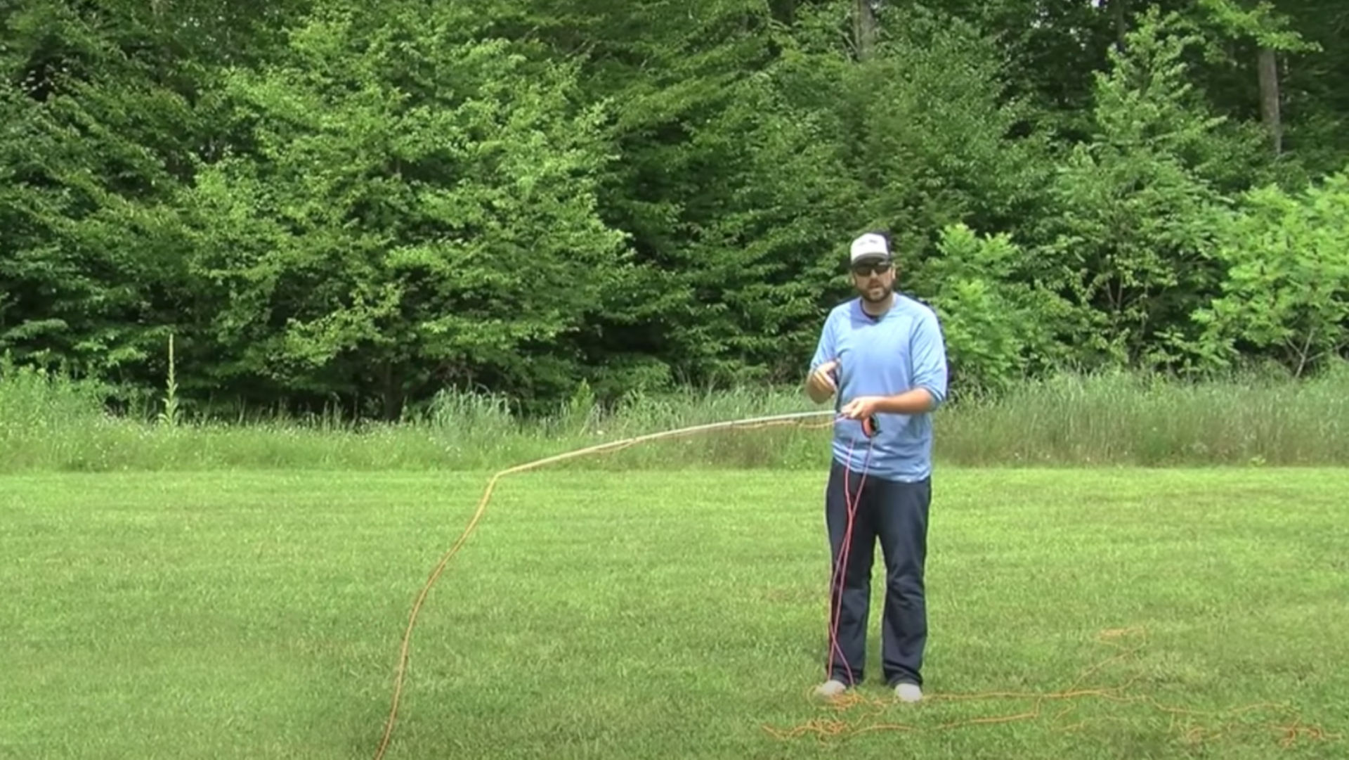 An instructor standing on grassy lawn holding a fly rod