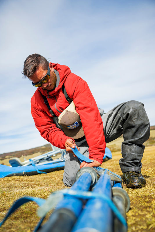 An angler in muddy waders kneels as they pack supplies