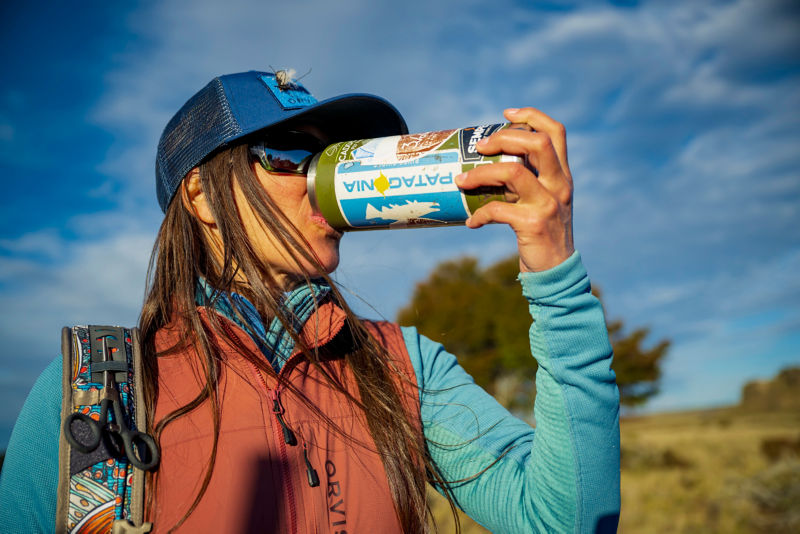 An angler with flies attached to a ball cap drinks water from a can