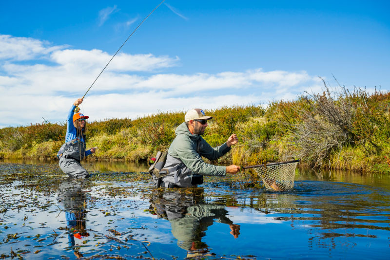 An angler lands a fish in a net wielded by another angler.