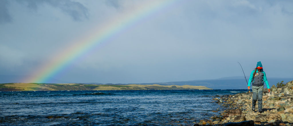 A rainbow rises from the hills and spreads over the ocean inlet