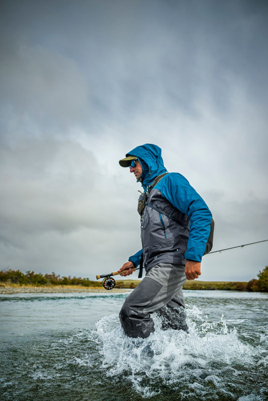 A man wades through a knee high river.