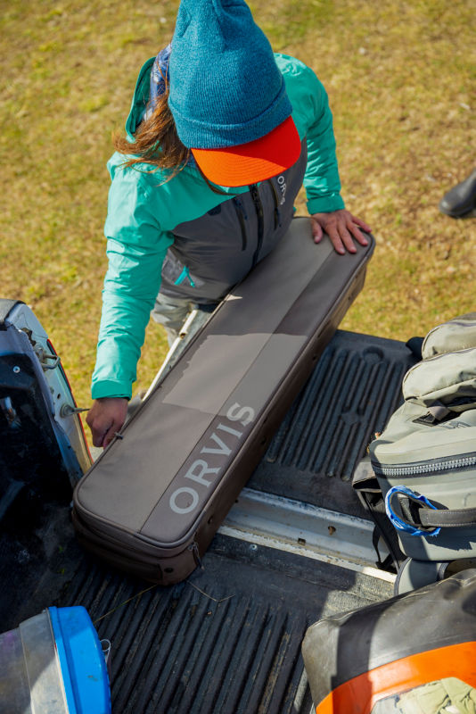 An angler zips up her travel bag in the trunk of her truck.