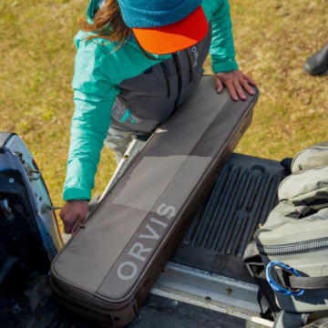 An angler zips up her travel bag in the trunk of her truck.