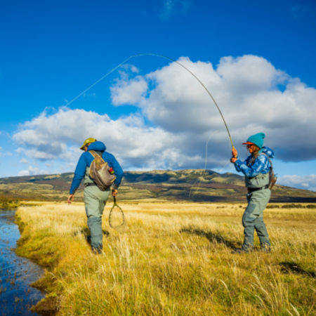 Two people fishing from the bank of a river in an open field 