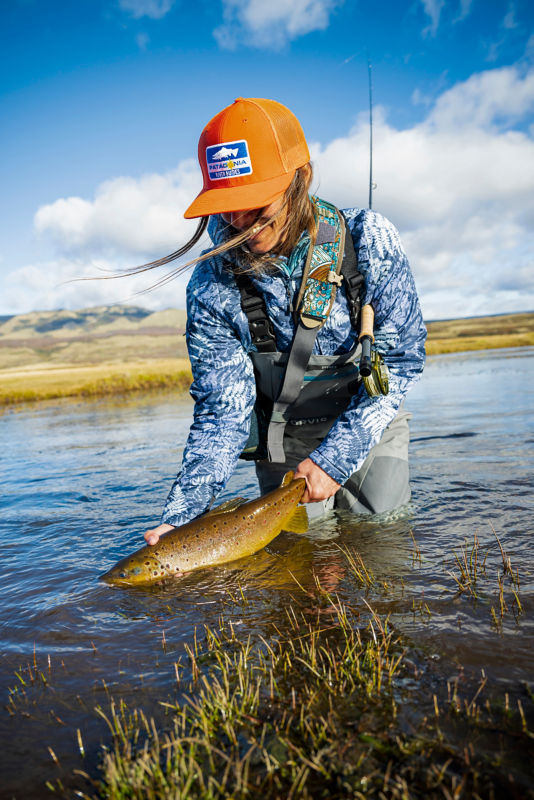 An angler holds her catch in the middle of a river.