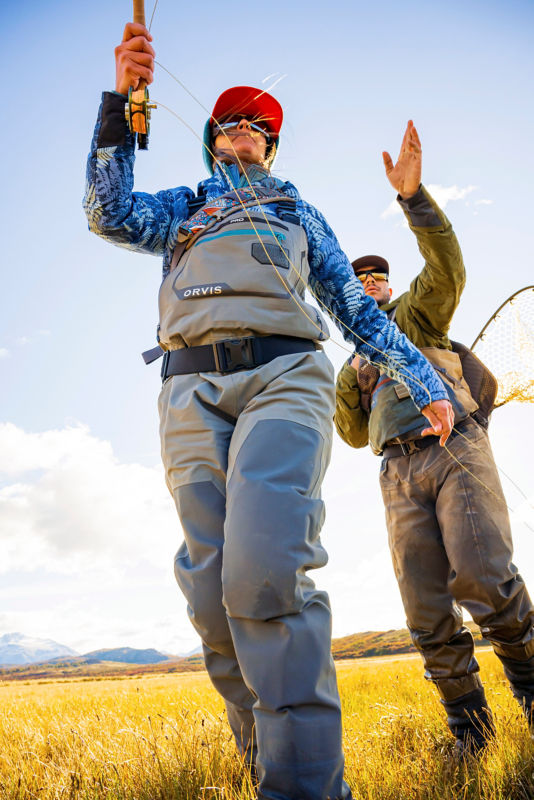 An angler casting guided by an instructor behind her.
