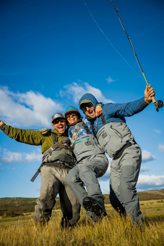 Three anglers in waders celebrate their day with hugs and smiles.