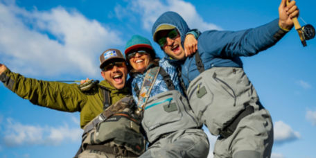 A group of people in fishing gear standing in a field smiling at the camera