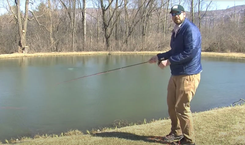 An instructor casting with a fly rod while standing next to pond
