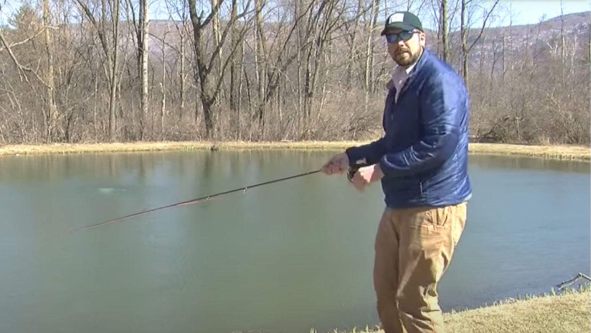 An instructor casting with a fly rod while standing next to pond