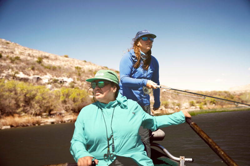 Two anglers in a boat work their way down a river.