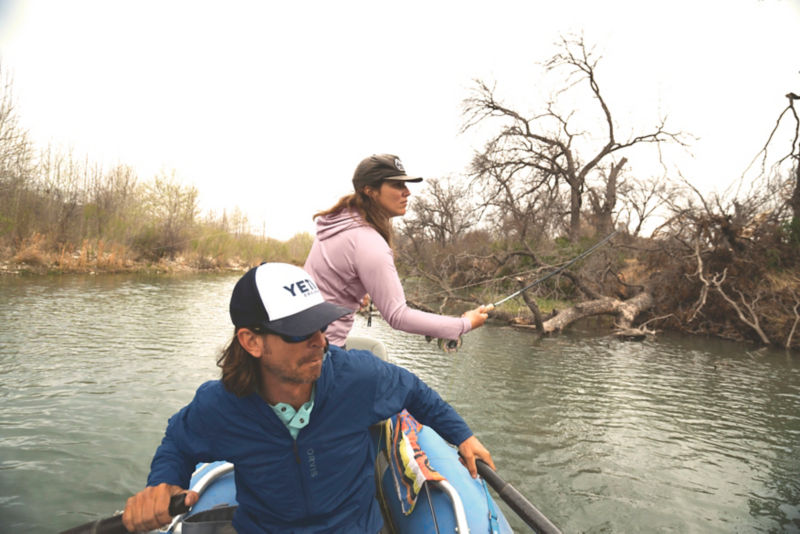 Two anglers in a rowboat fishing a river.