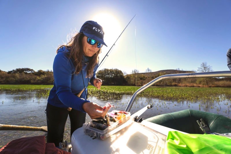 An angler in a ball cap chooses a fly from a box in a boat