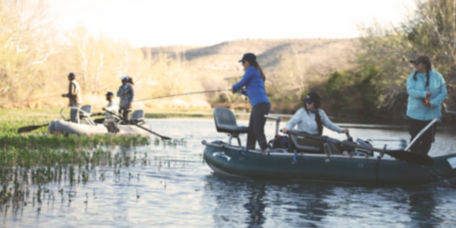 A group of anglers fishing together from float rafts on a river