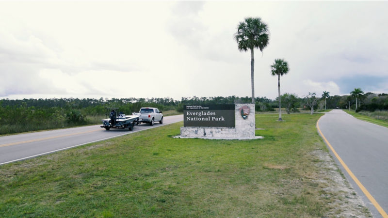 A truck hauling a small motor boat drives past the Everglades National Park sign