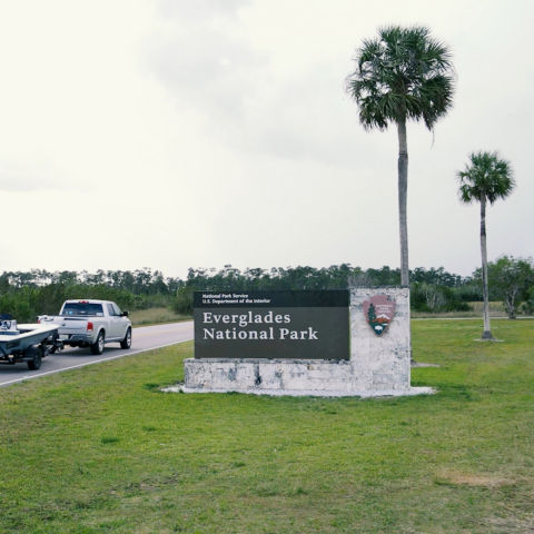 A truck hauling a small motor boat drives past the Everglades National Park sign