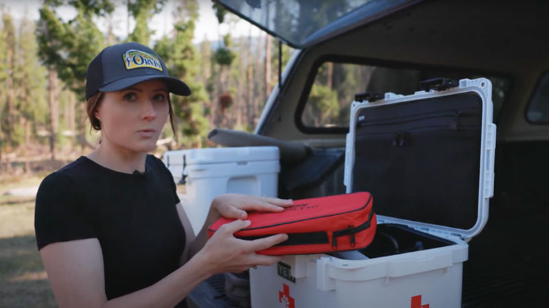 A woman holding up a first aid pouch that contains bandages