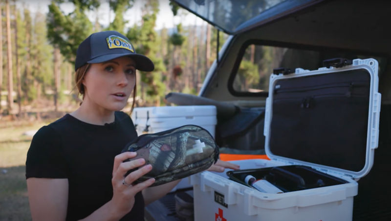 A woman holding up a small camo medicine bag at the back of her truck